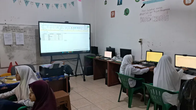 Siswa berlatih menggunakan komputer dengan materi lembar kerja ditampilkan di depan kelas.